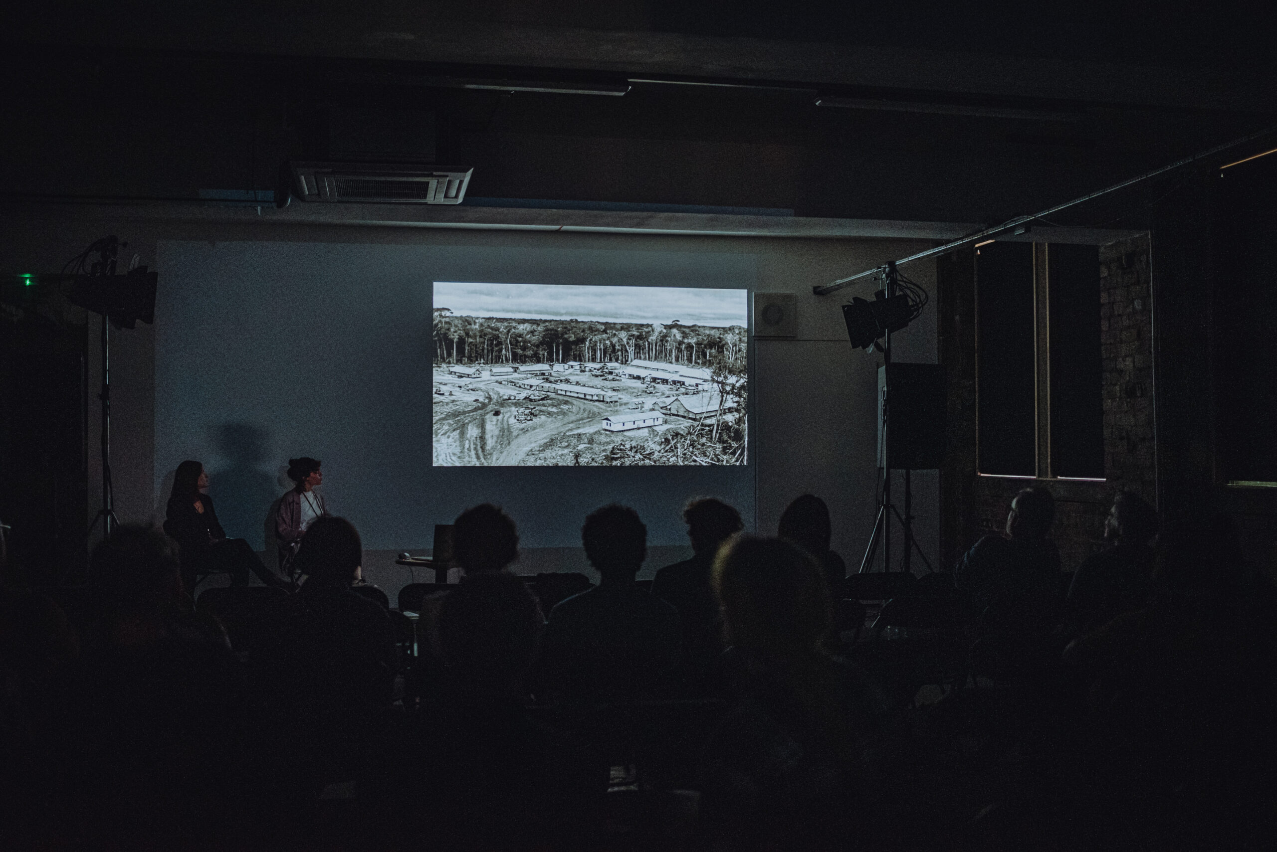 Photo from Glasgow Short Film Festival 2022 when Civic House was booked as a Festival Hub. The photo shows a darkened venue space illuminated by a projection of a film onto one white wall. There are the silhouettes of presenters and audience in the foreground.