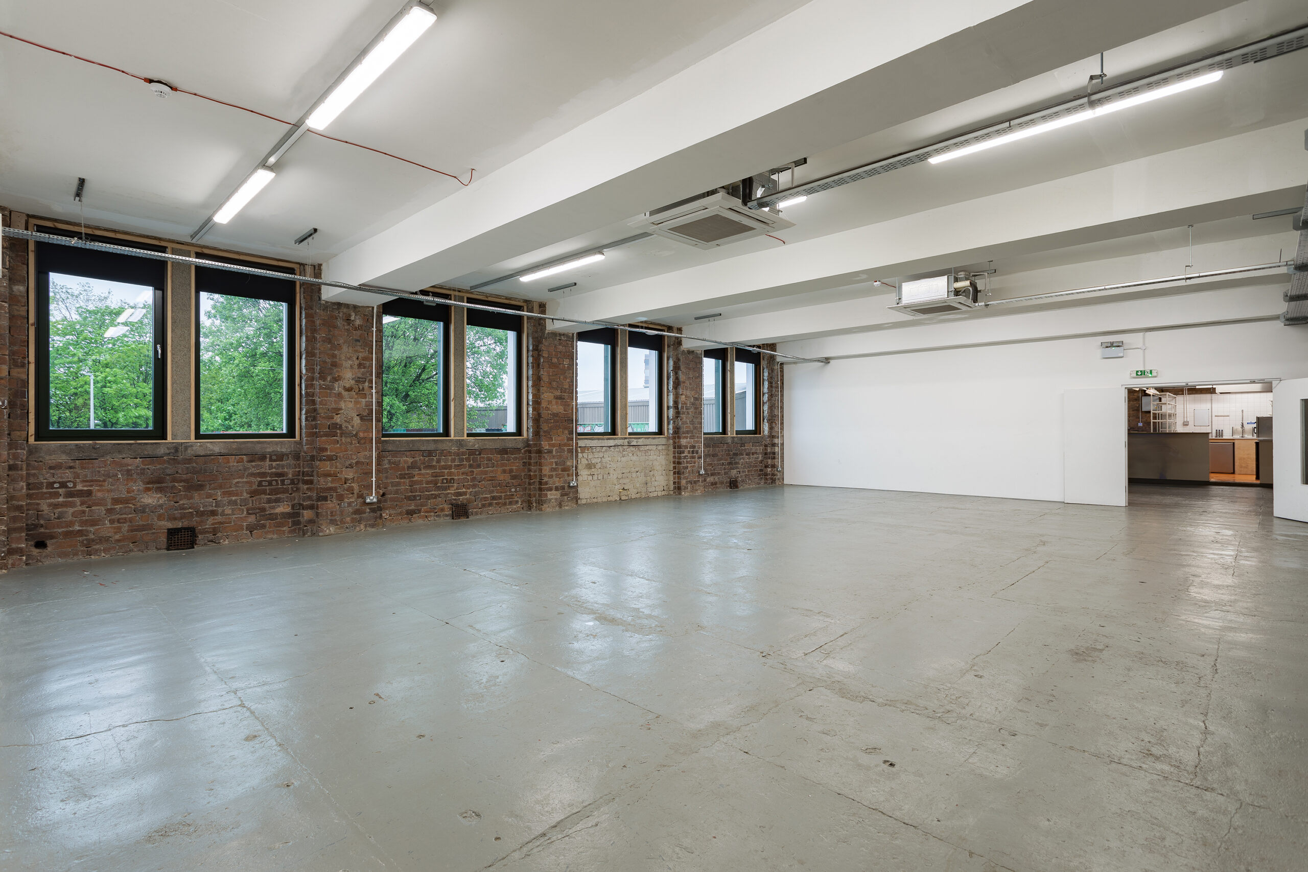 Photo of the venue space at Civic House looking towards the street. This can be used as an afterparty or screening space for the Festival hub as it is a spacious industrial space with natural light from windows on the left of the room and visible brickwork.