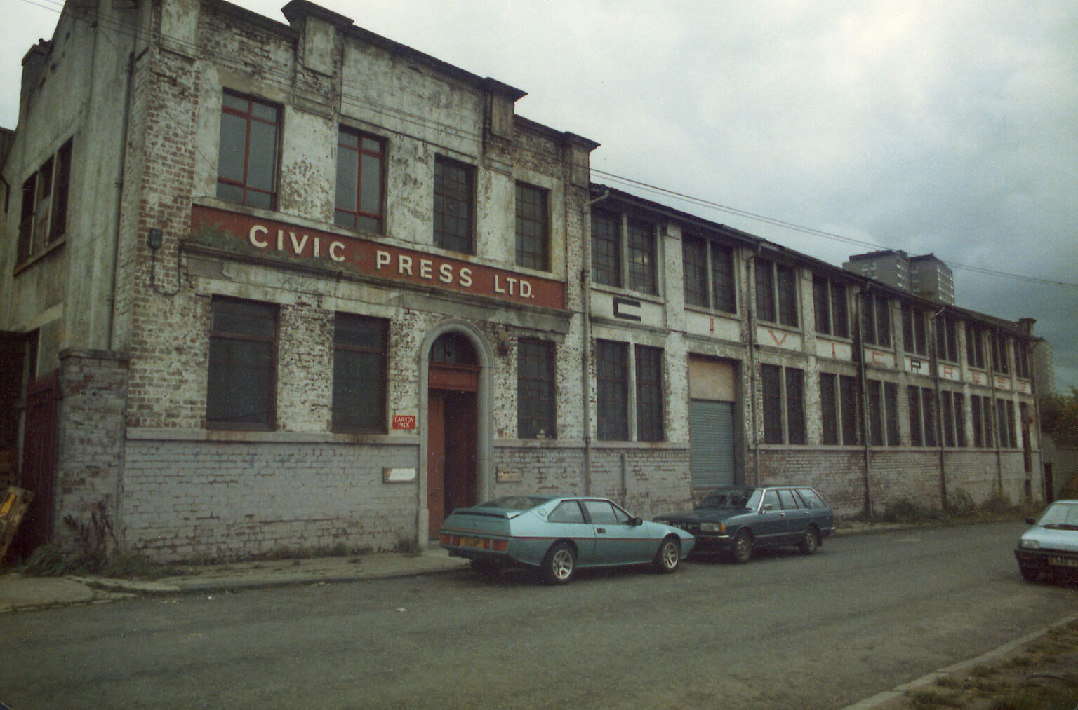 Archival photo of Civic House when it was Civic Press, a left wing publishing house in Glasgow. The iconic sign on the facade of the building reads "Civic Press" and a matching sign reads "Civic Press Ltd." above the front door. There are two cars circa 1970 that hint to the date the photo was taken.