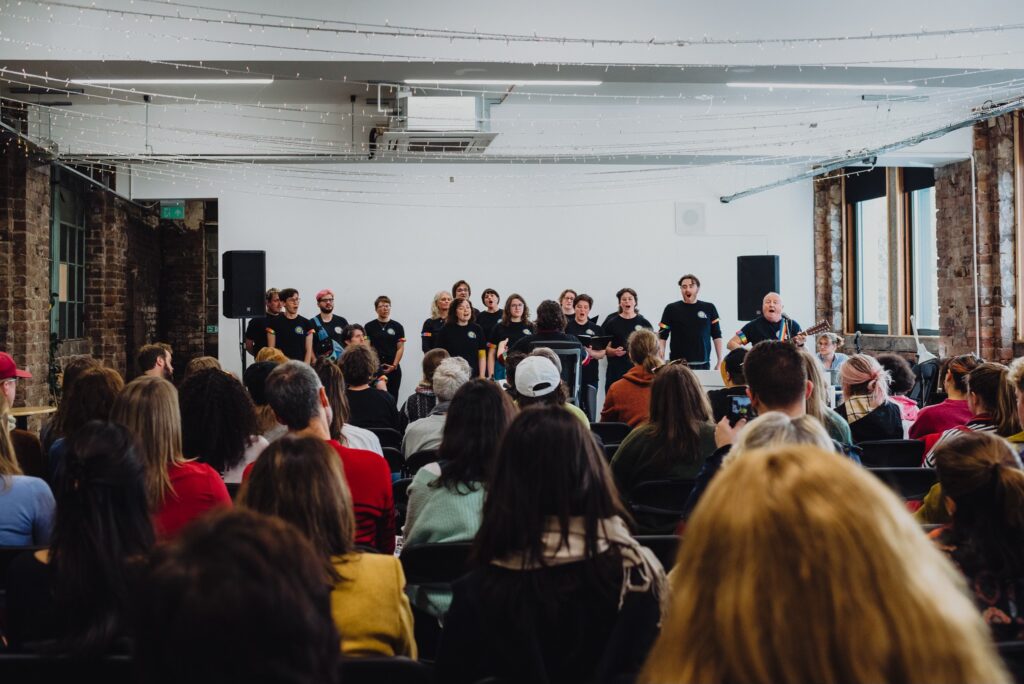 People sit in rows in Civic House Venue watch Quoir a Glasgow based Queer choir perform.